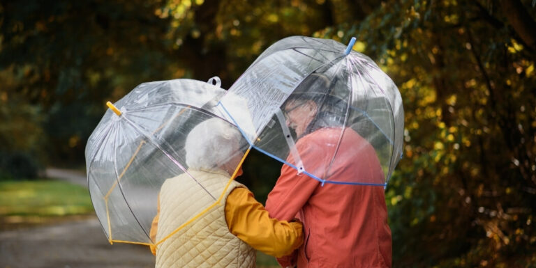 Elderly Couple Walking Outdoors with Umbrellas in the Rain at a Memory Care Facility